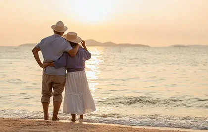 aged couple looking at the sunset by the beach